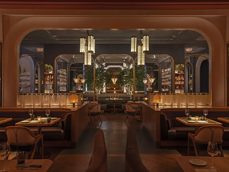 A dining room seen through a wide arch, with brass pendant lights, banquettes and trees beyond