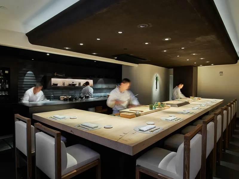Chefs working behind a long pale wood counter lined with white chairs