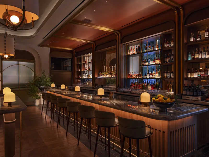 A restaurant bar with a marble counter, lit back shelving and table lamps along the bar