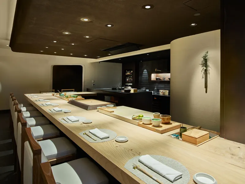 A pale wood chef's counter set for service under a dark ceiling