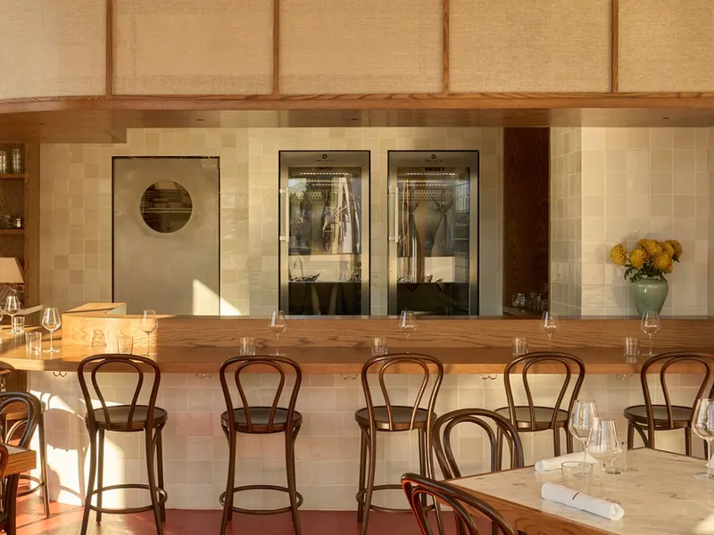 A bar with bentwood stools in front of tiled walls and wine cabinets