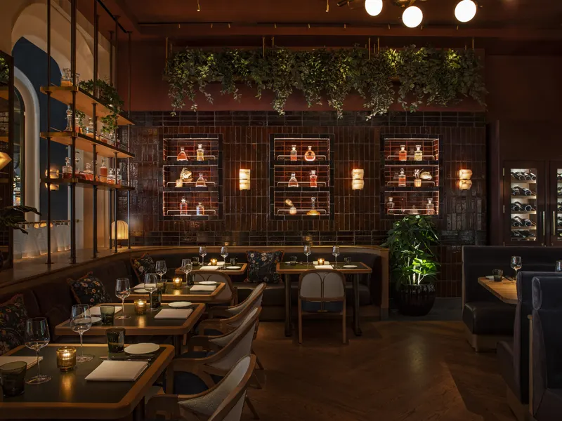A dining room with a planted ceiling and lit shelving over leather banquettes