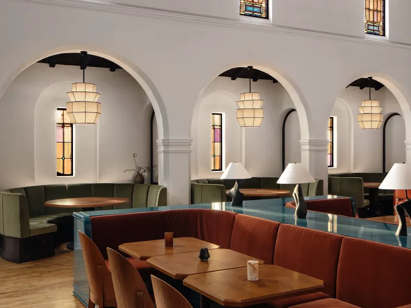 A dining room of curved banquettes under white arches and stained glass windows