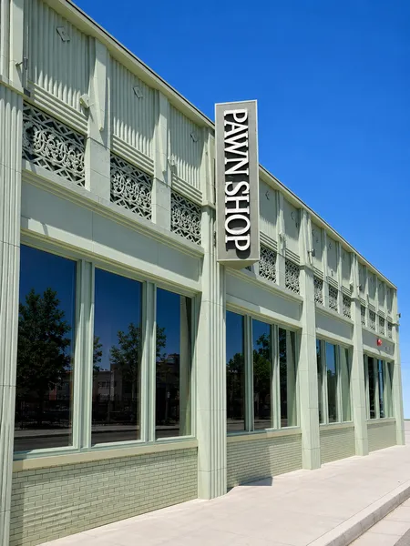 A pale green two-story building with a vertical blade sign, seen from the sidewalk