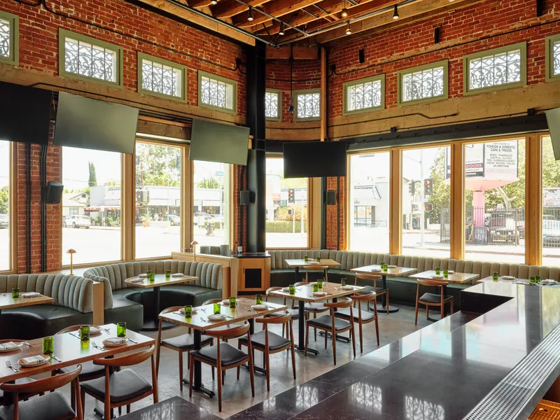 A dining room of booths and timber tables under high windows in a brick building