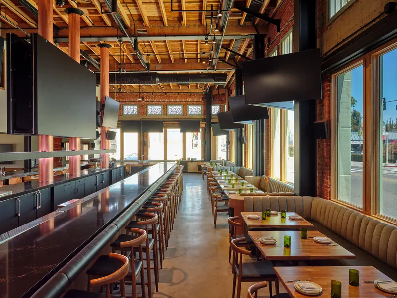 A long bar and banquette dining room under exposed timber joists in a brick building