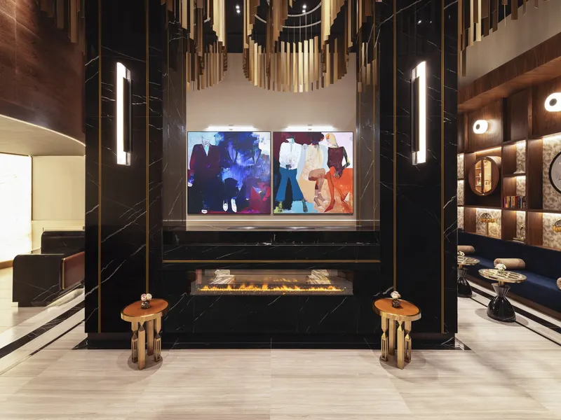 A hotel lobby with a fireplace set into a black marble wall under a brass ceiling feature