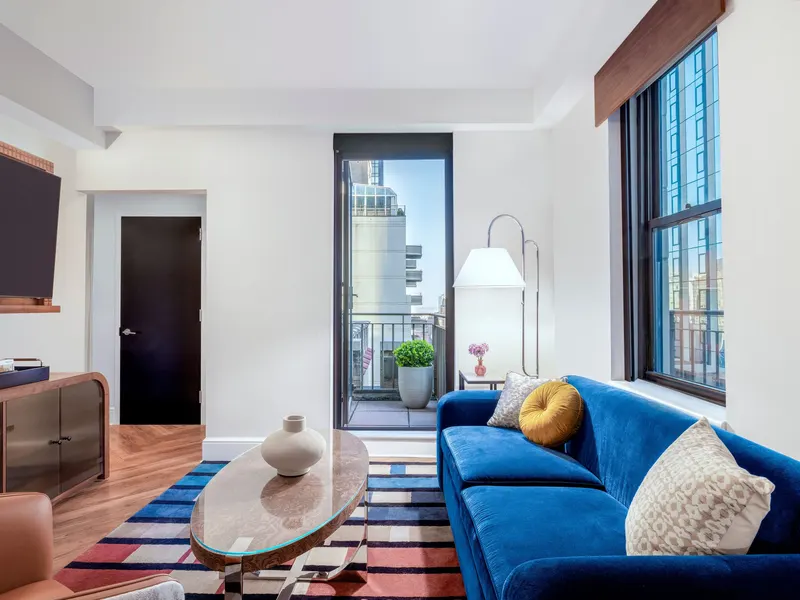 A hotel suite living area with a blue sofa and a door to a balcony