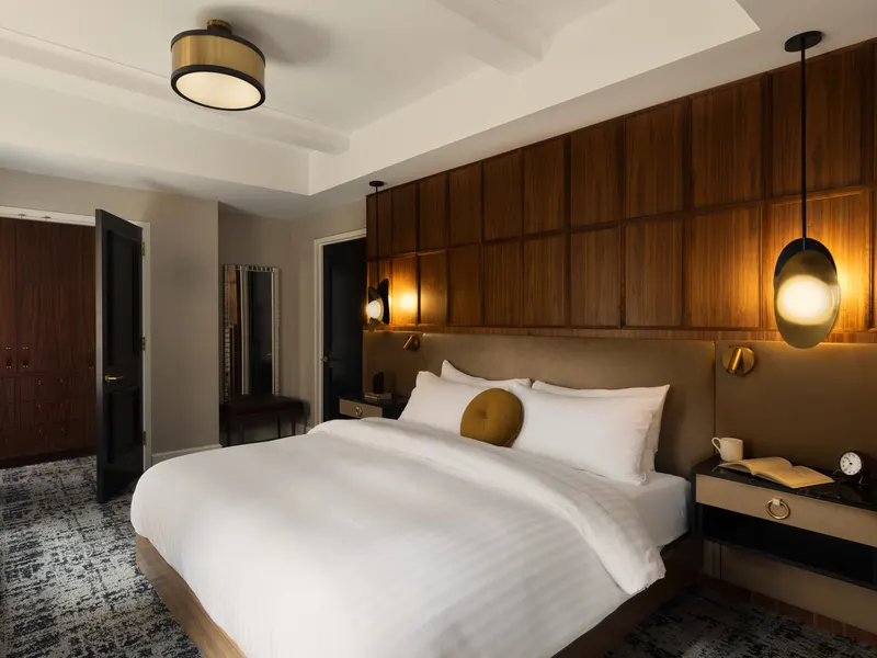 A hotel guest room with a walnut paneled wall behind the bed