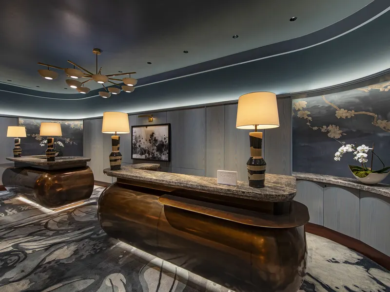 A hotel lounge with a curved bronze bar, a marble floor and table lamps