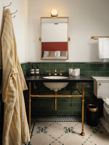 A hotel bathroom with green tile, a brass washstand and a striped robe