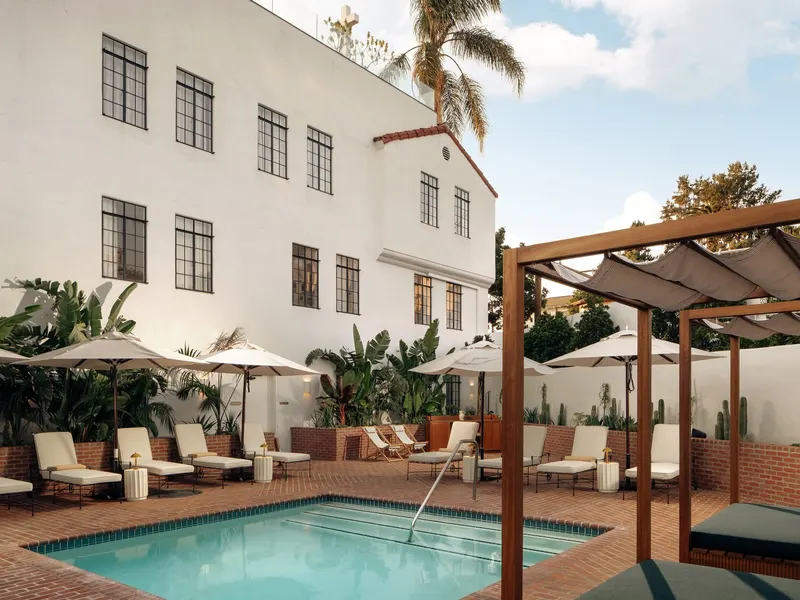 A hotel courtyard with a pool, lounge chairs and a timber pergola against white walls
