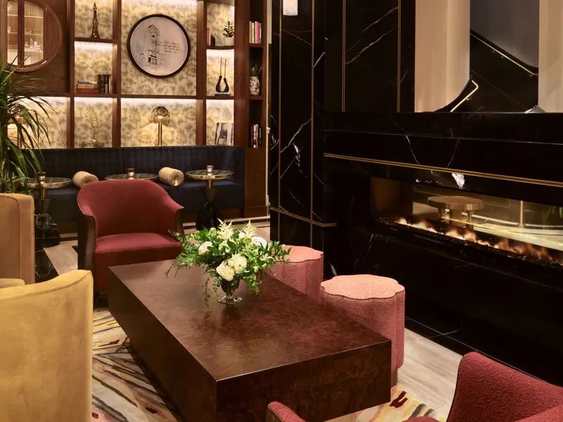 A hotel lounge with velvet armchairs and a fireplace in a black marble wall