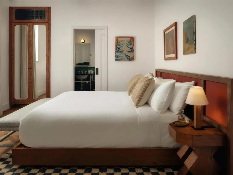 A hotel guest room with a timber bed, white linens and framed prints