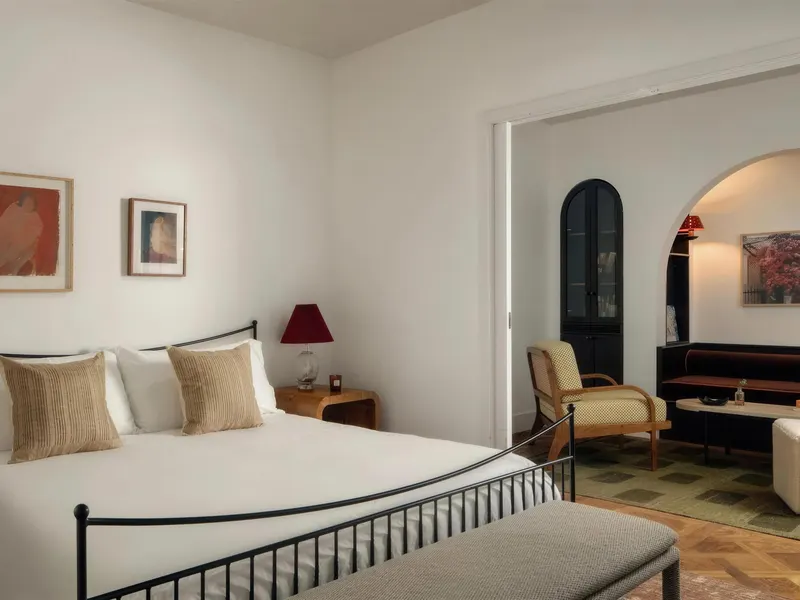 A hotel bedroom with an iron bed frame, opening through an arch to a sitting area
