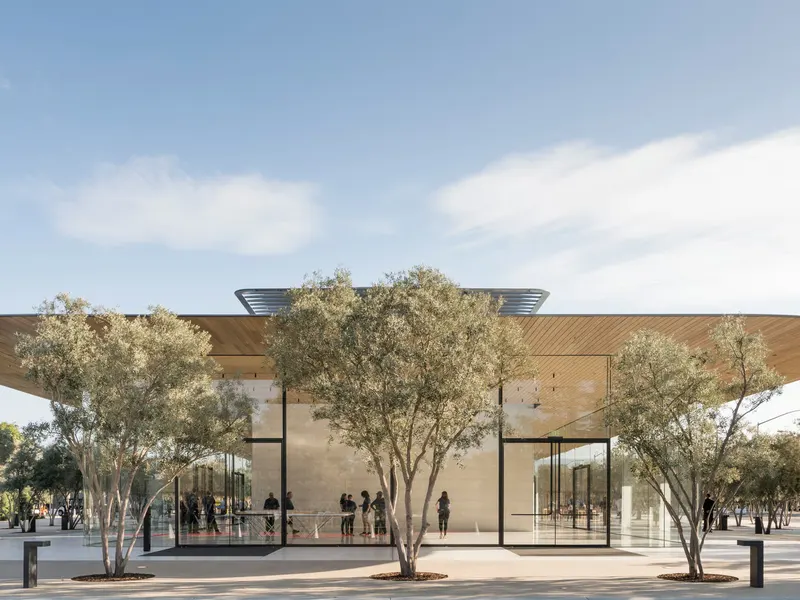 A glass pavilion under a wide flat roof, with olive trees in front