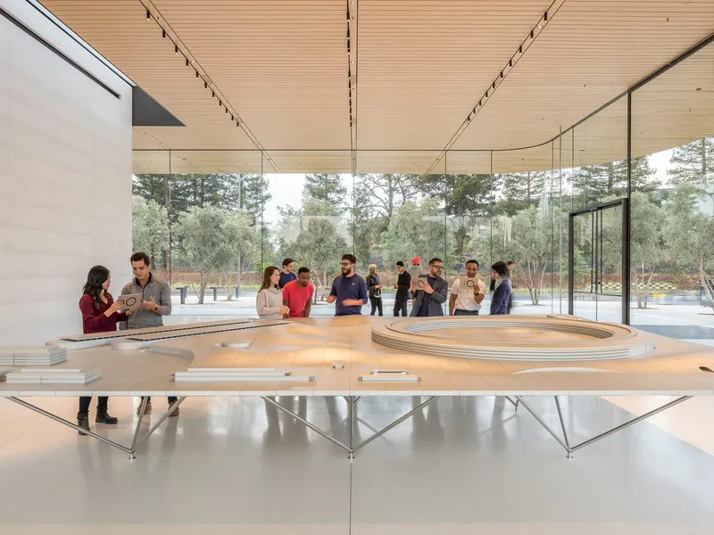 A glass-walled room with a large white site model and visitors around it