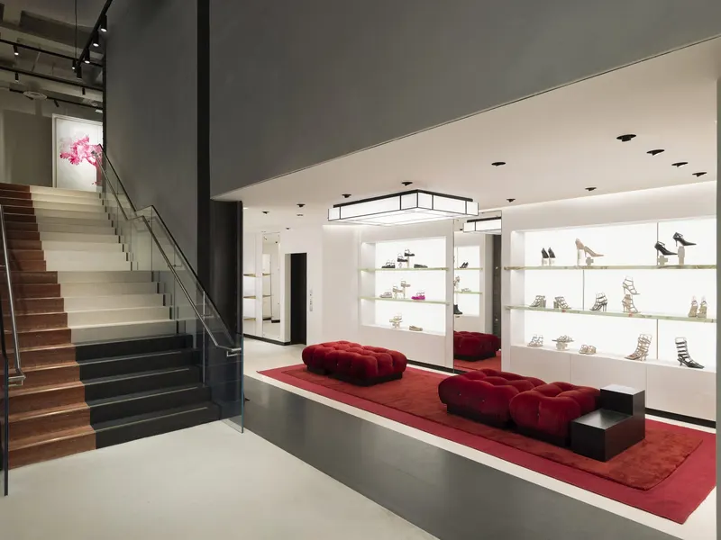 A shoe salon with a stair, lit wall shelving and red ottomans