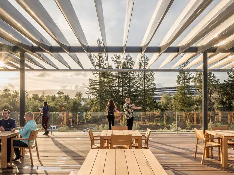 A rooftop terrace under a slatted canopy, with timber tables and a view to trees