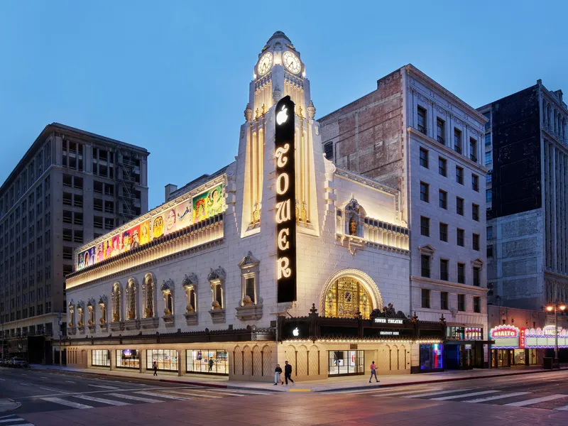 A restored historic theater on a downtown street corner at dusk, its marquee and clock tower lit