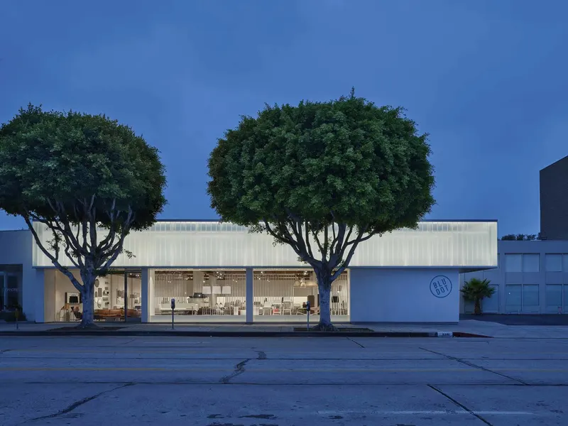 A low white showroom building at dusk behind two round clipped trees