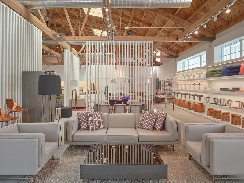 A furniture showroom with gray sofas under timber trusses and a slatted screen