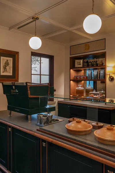 A shop counter with a green leather chair, timber shelving and coffee goods