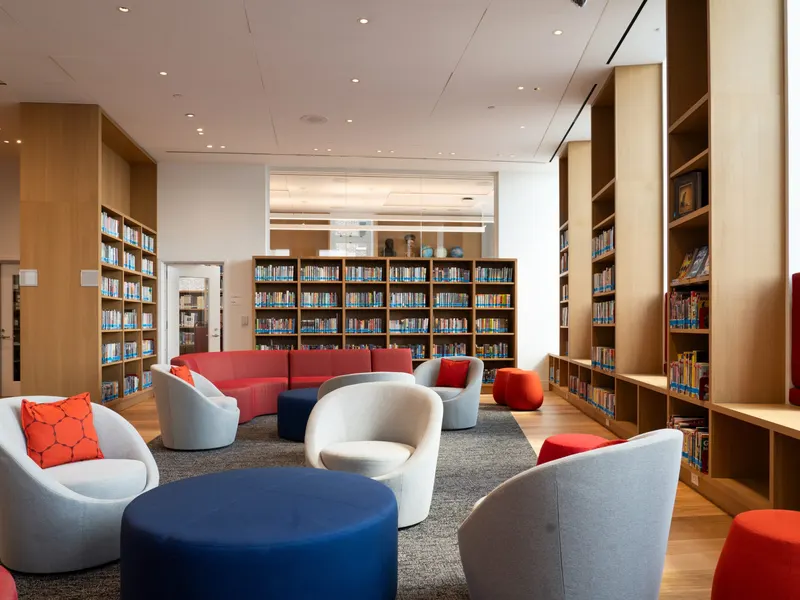 A library lounge with white swivel chairs, a red sofa and timber bookshelves
