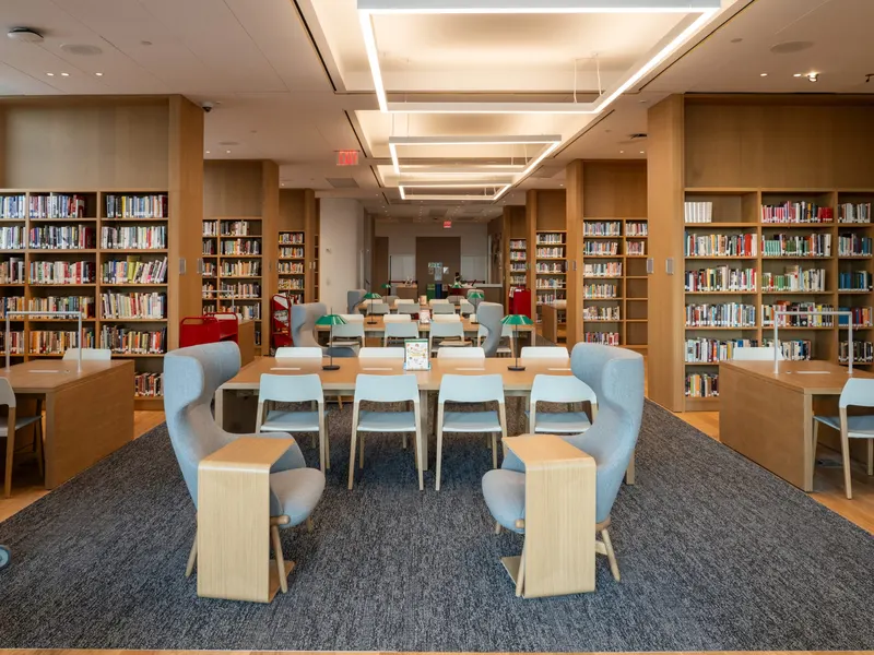 A library reading room with study tables, pale blue chairs and full bookshelves
