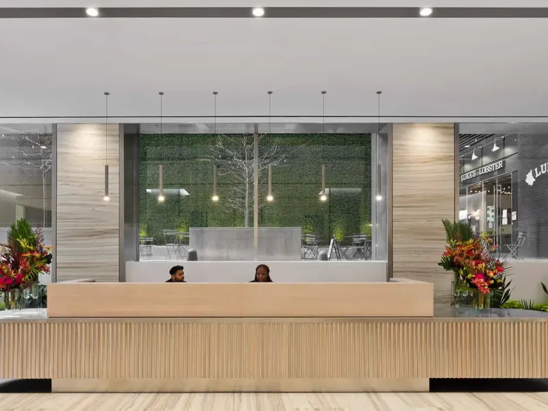 An office lobby with a fluted wood reception desk, a planted wall behind it and flowers at each end