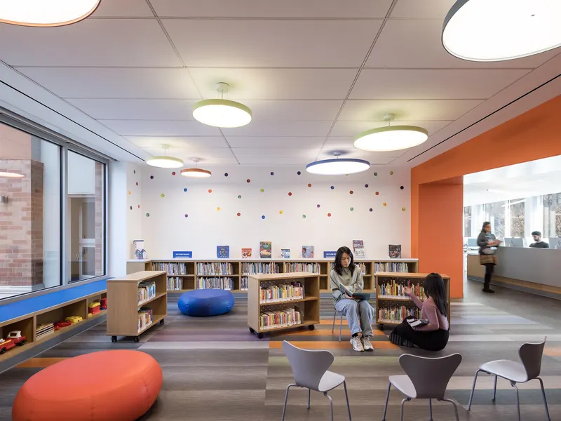 A children's library with an orange wall, low shelving and floor cushions