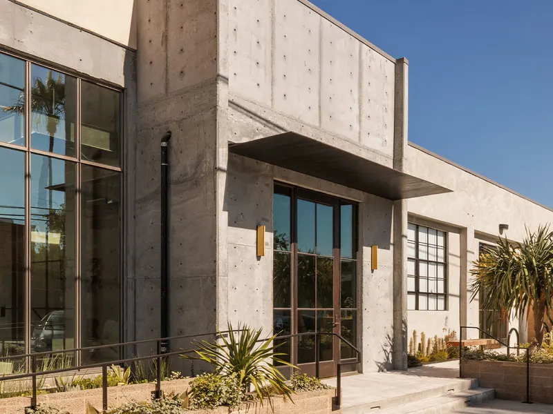A board-formed concrete office building with tall steel-framed windows and desert planting
