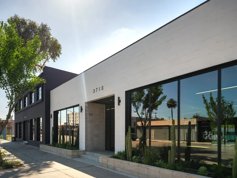 A white block building with large black-framed windows along a planted sidewalk