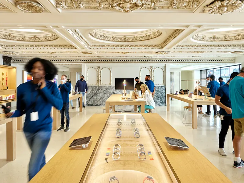 A store floor with timber display tables under an ornate plaster ceiling, with staff and visitors