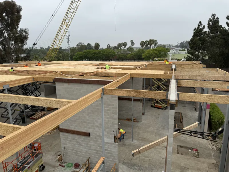 New glulam beams and roof framing set on block walls, with a crane beyond
