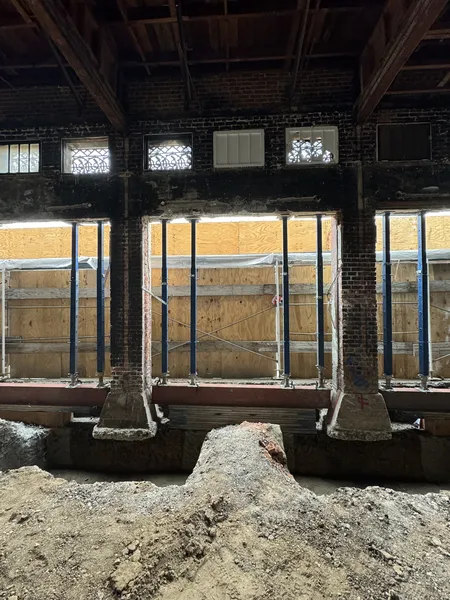Steel shoring braced against brick piers and a boarded opening during structural work