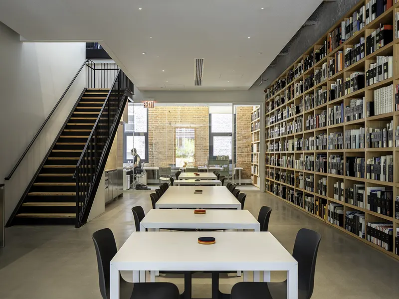 An office library with a black steel stair, long white tables and a full-height bookshelf wall