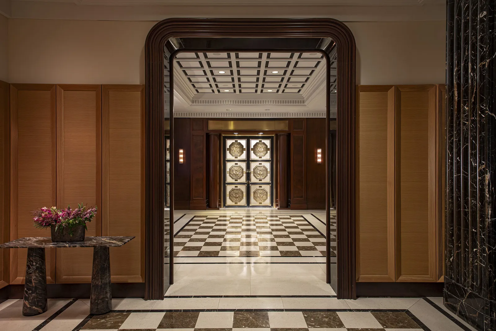 A hotel lobby with a checkered marble floor, seen through a dark stone portal