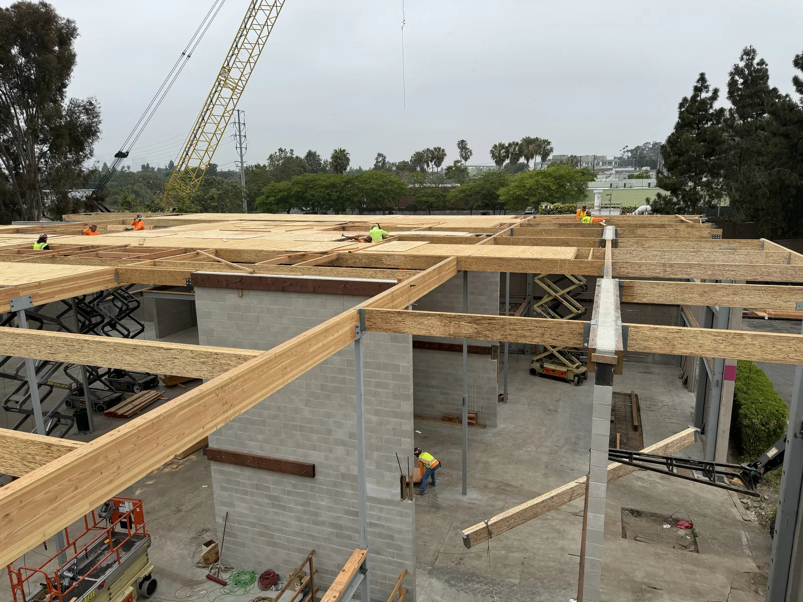 New glulam beams and roof framing set on block walls, with a crane beyond