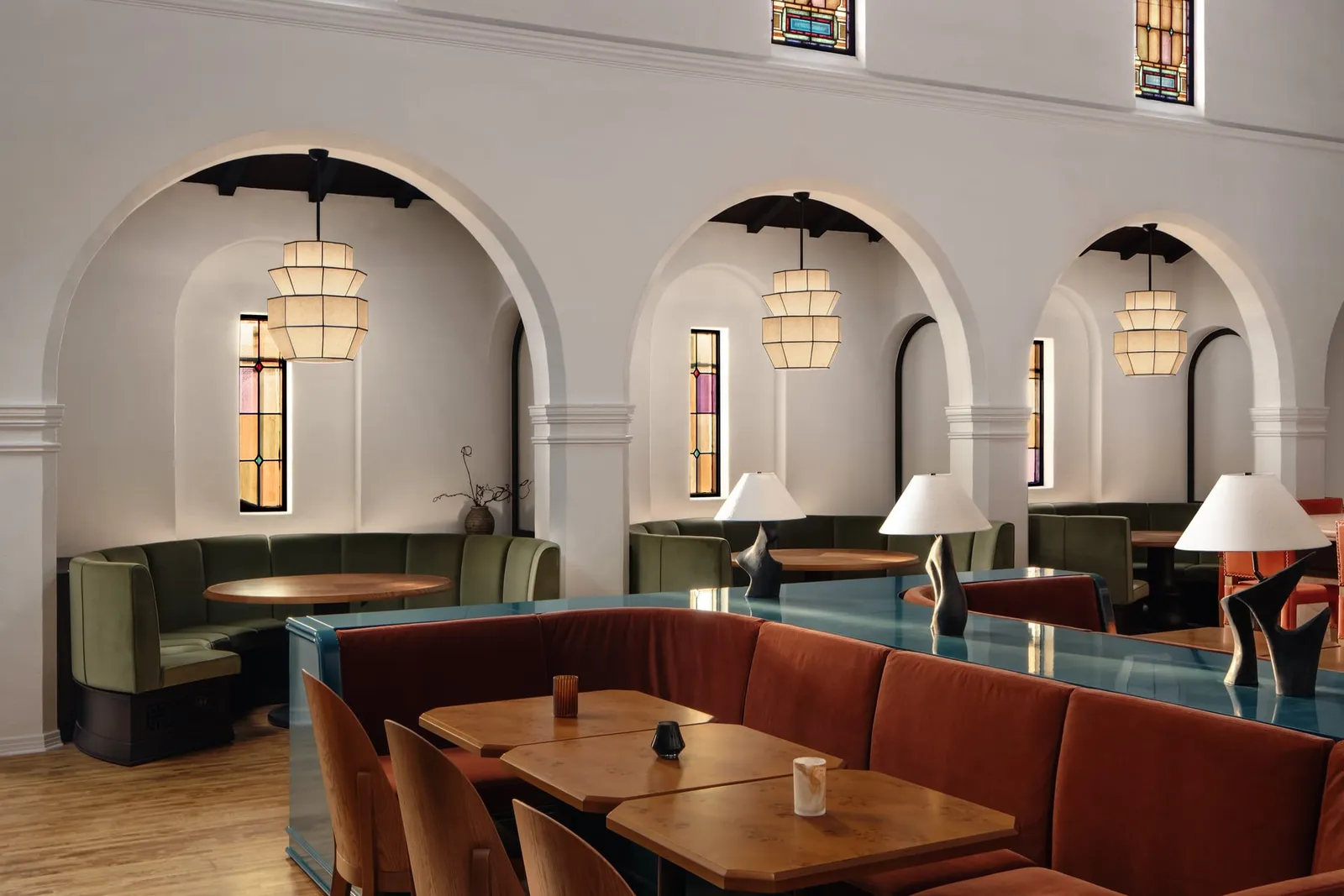 A dining room of curved banquettes under white arches and stained glass windows