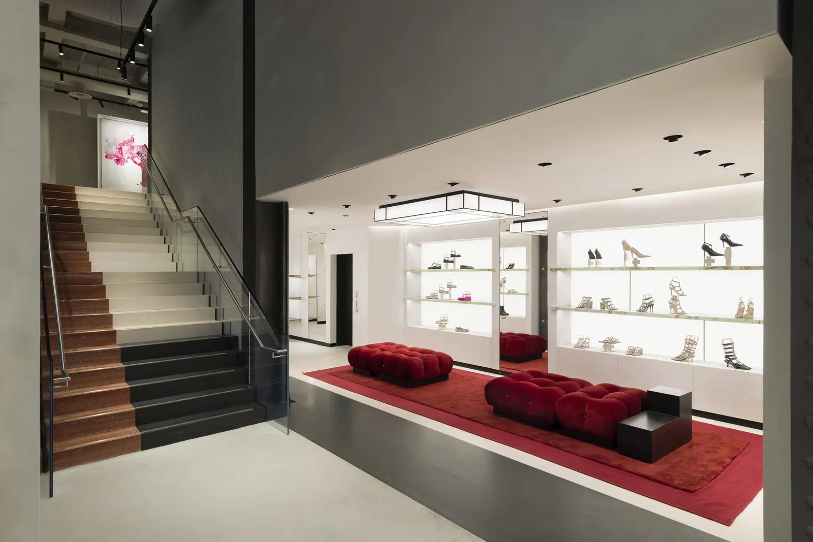 A boutique with a stair and red seating beside lit shoe displays