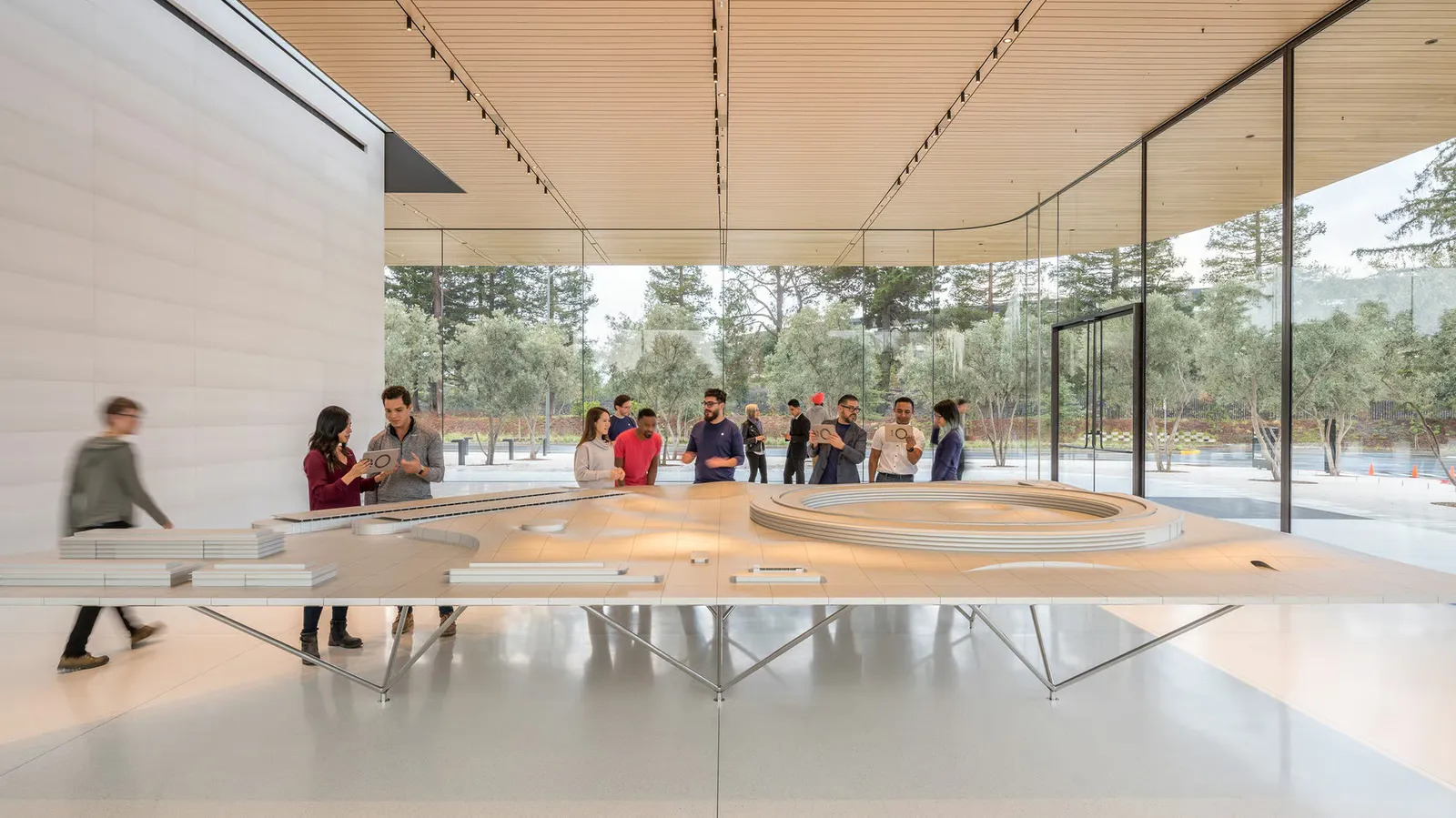 Visitors around a large site model in a glass pavilion with a timber ceiling