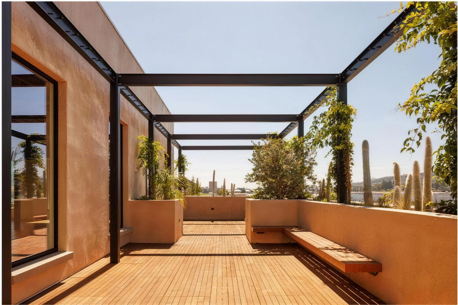 A roof terrace under a steel pergola with planters and timber decking